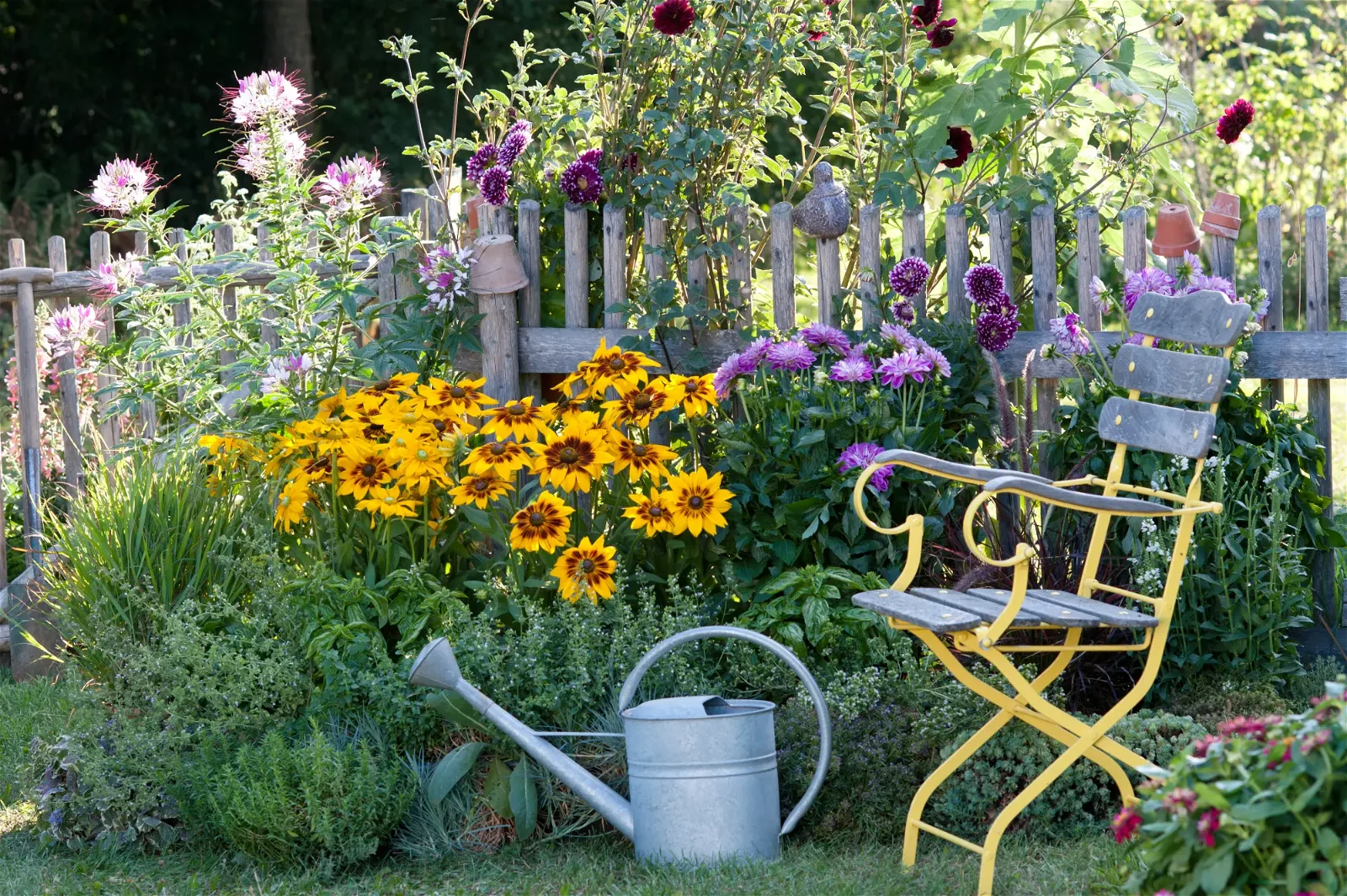 Bunter Garten mit blühenden Sommerblumen, Gießkanne und Gartenstuhl