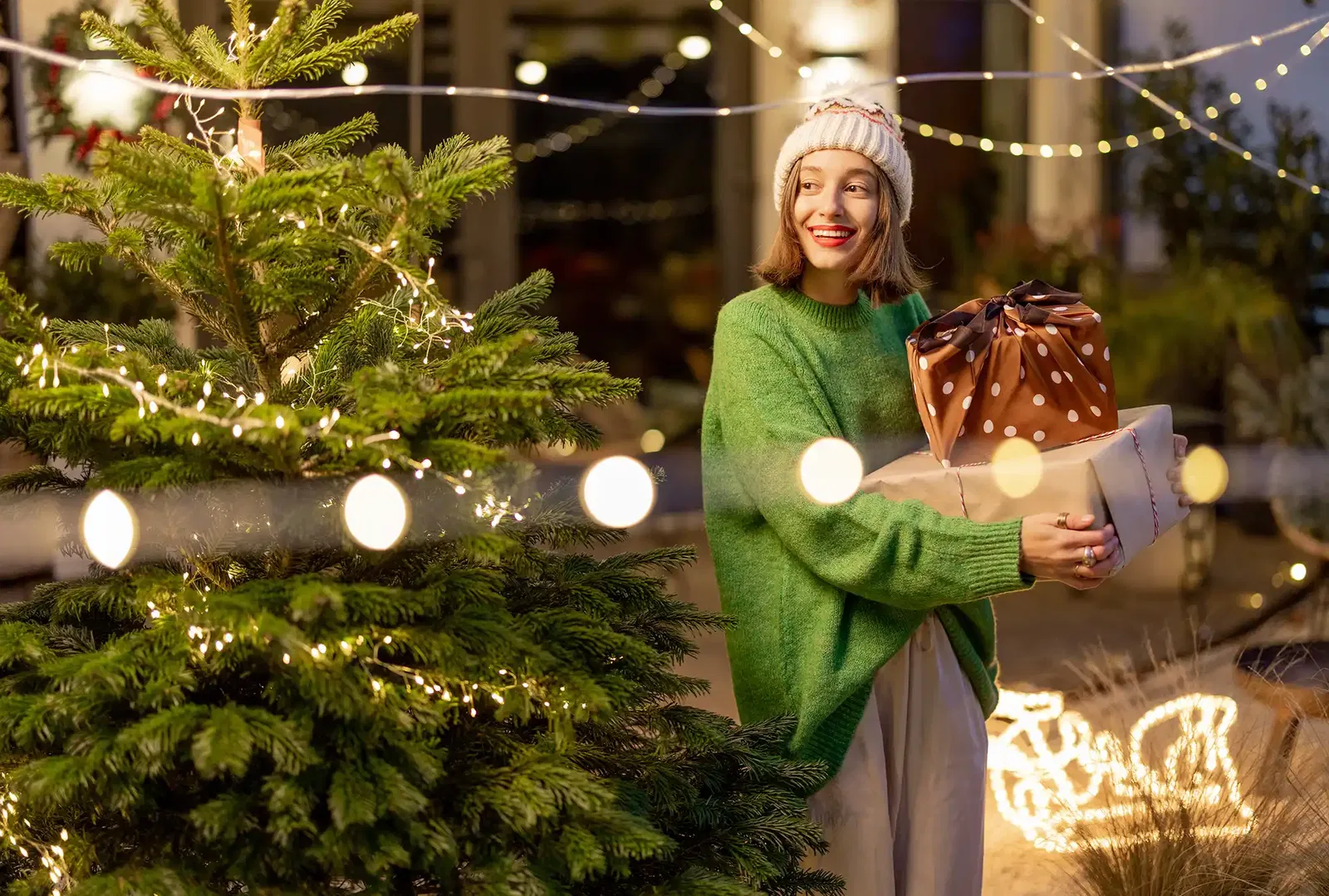 Frau am Weihnachtsbaum im Garten mit Geschenken im Arm 