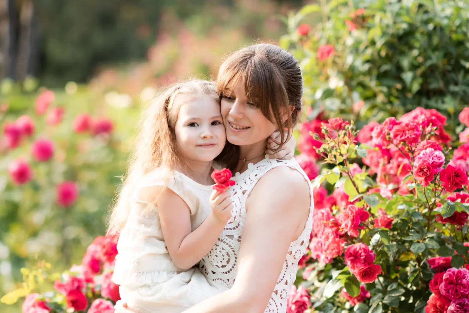 Junge Mutter mit Tochter auf dem Arm stehen in einem blühenden Rosengarten