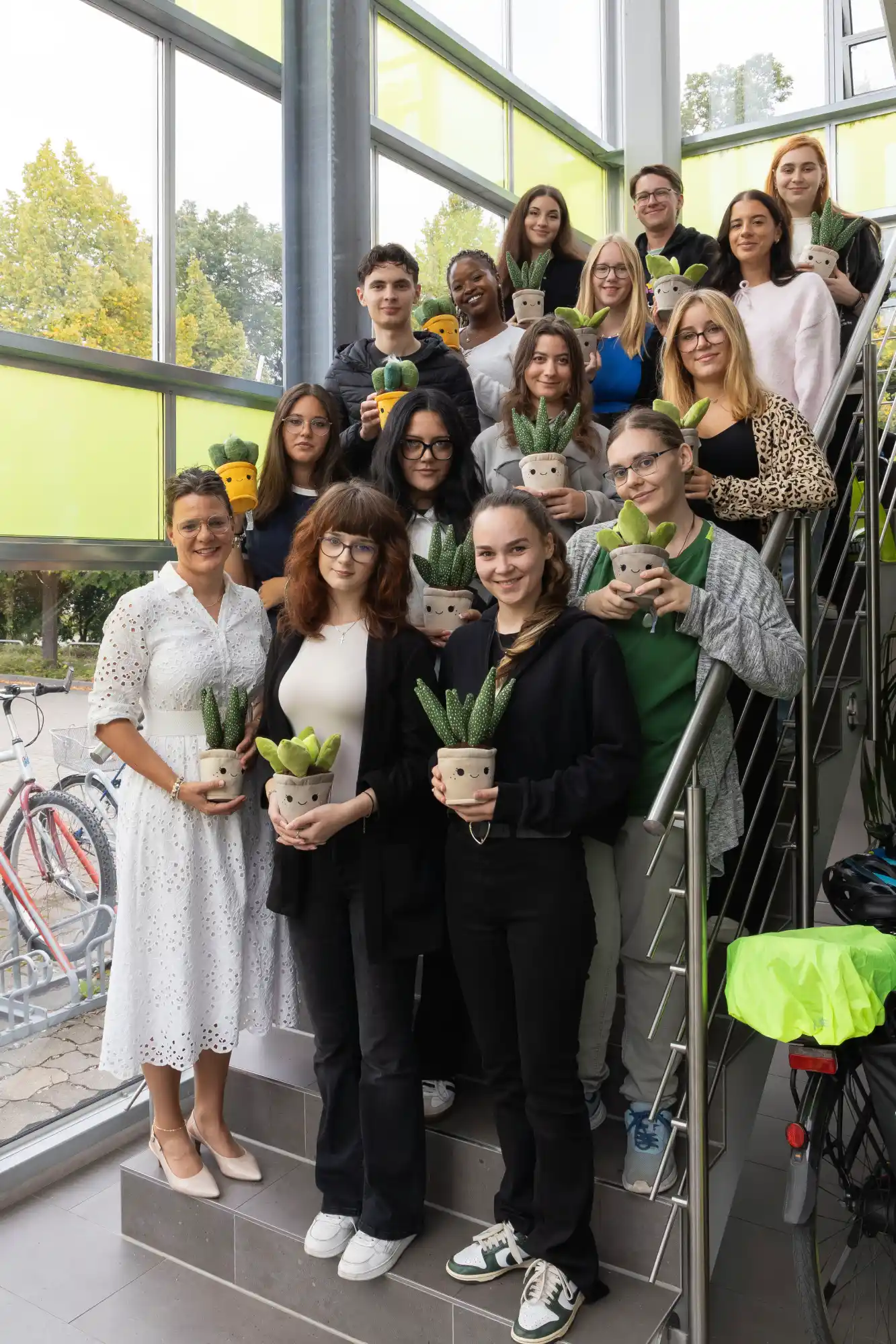Die vierzehn neuen Azubis aus Heilbronn stehen mit Sukkulenten im Treppenhaus vom DLZ